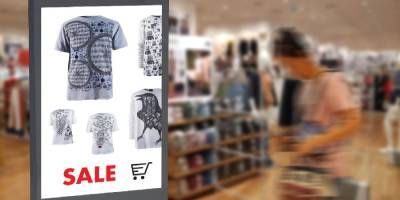 Una mujer está comprando en una tienda de ropa y mirando un cartel de oferta.