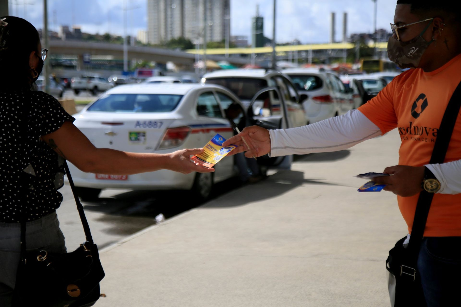 Un hombre con una camisa naranja le está dando un volante a una mujer.
