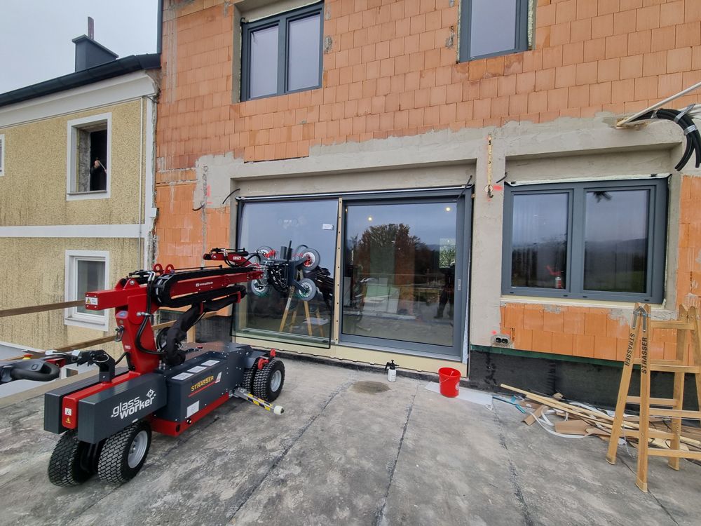 Roter Glasheberroboter installiert ein großes Fenster neben einem Backsteingebäude.