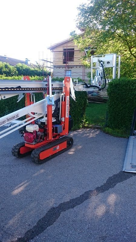 Eine kleine orange-weiße Maschine steht vor einem Haus.