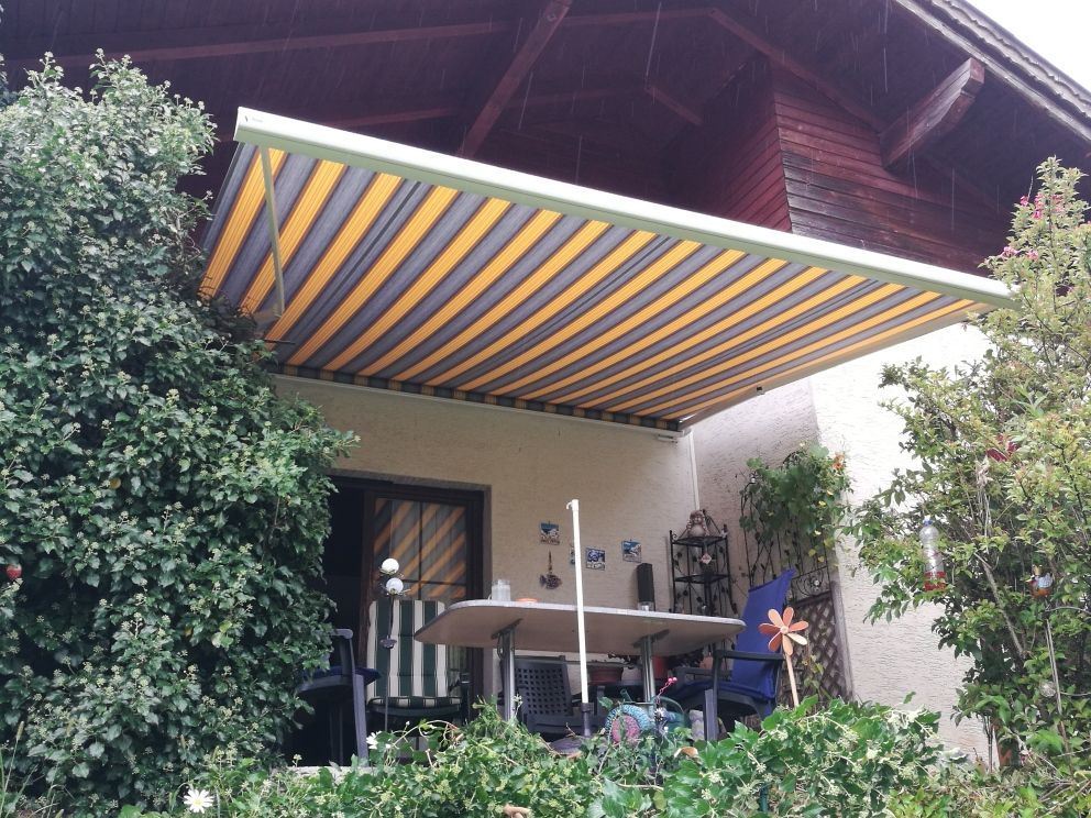 Eine Terrasse mit einer gelben und grauen Markise darüber