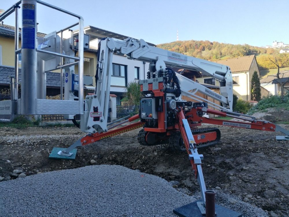 Vor einem Gebäude steht ein Kran im Dreck.