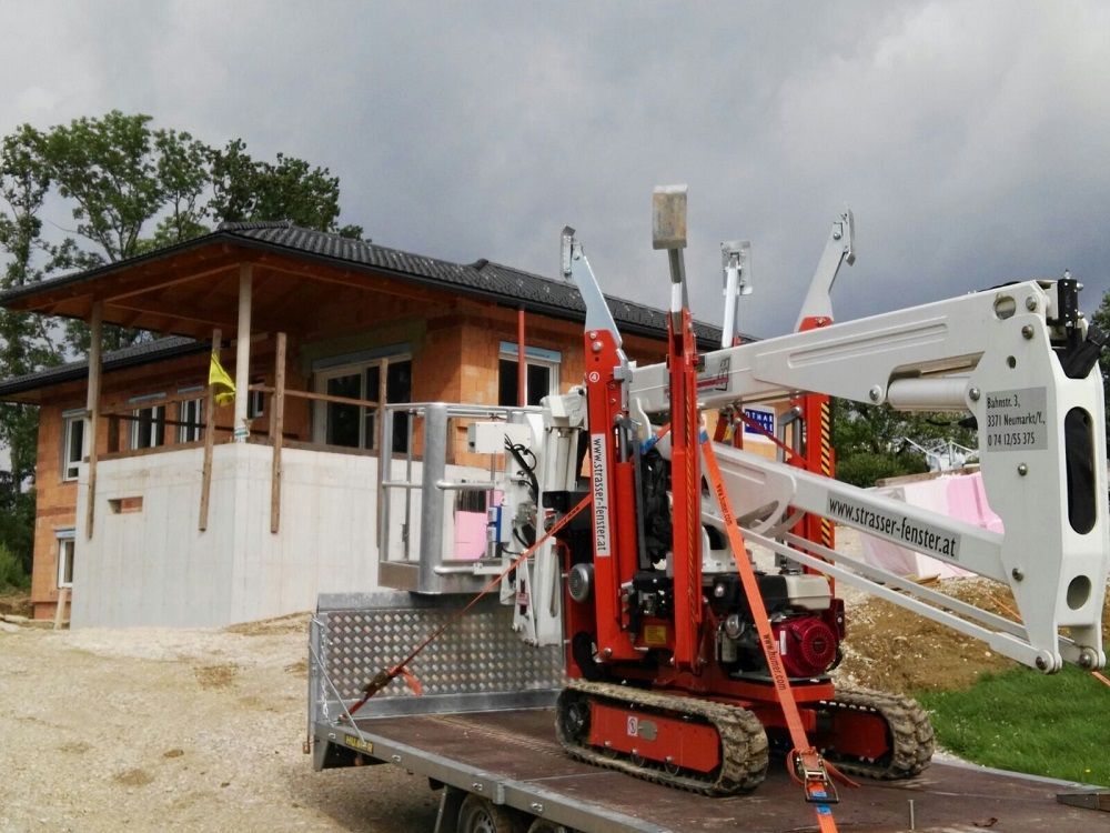 Vor einem im Bau befindlichen Haus steht auf der Ladefläche eines Lastwagens ein Kran.