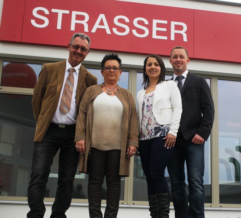 Eine Gruppe von Menschen steht vor einem Schild mit der Aufschrift „Strasser“