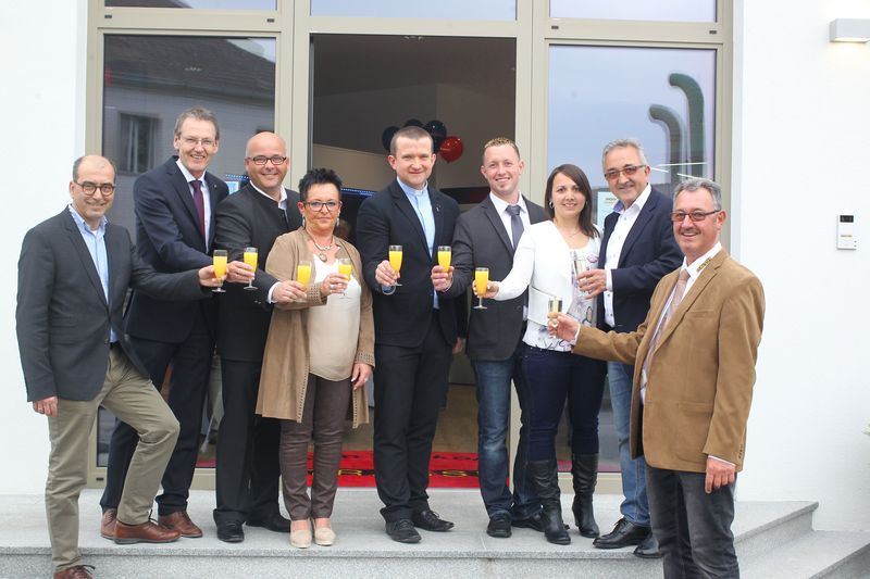 Eine Gruppe von Menschen steht mit Champagnergläsern in den Händen vor einem Gebäude.