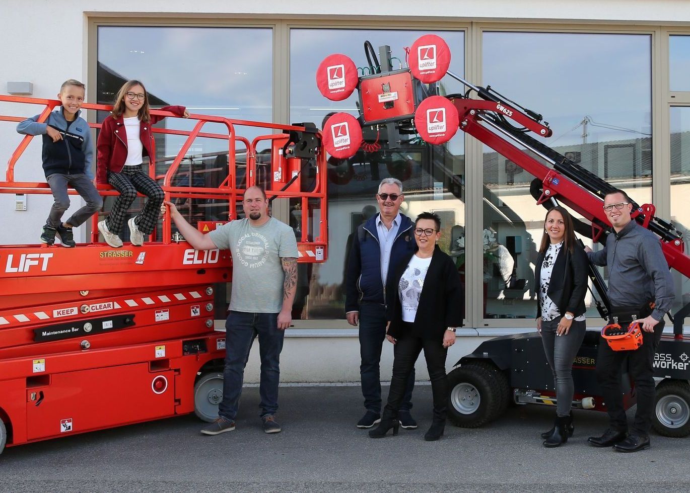 Menschengruppe bei roten Baumaschinen. Zwei Kinder auf Hebebühne, Erwachsene posieren bei Maschinen.
