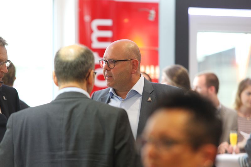 Ein Mann im Anzug und mit Brille spricht in einer Menschenmenge mit einem anderen Mann.