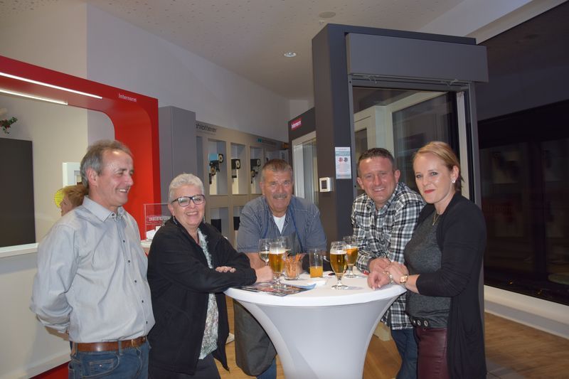 Eine Gruppe von Leuten steht mit Gläsern Bier um einen Tisch herum.