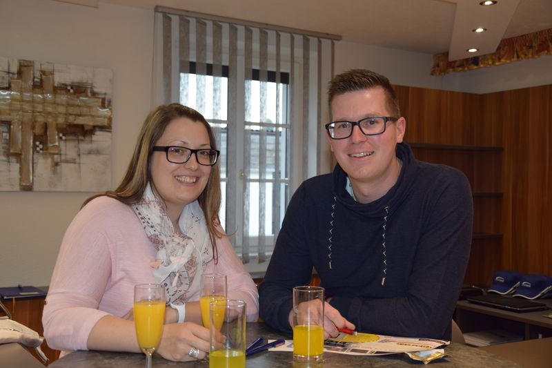 Ein Mann und eine Frau sitzen mit Gläsern Orangensaft an einem Tisch.
