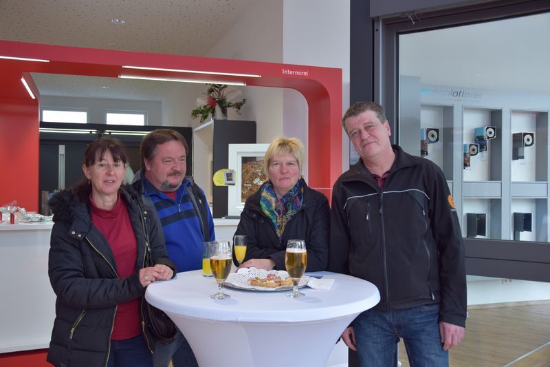 Eine Gruppe von Leuten steht mit Gläsern Bier um einen Tisch herum.