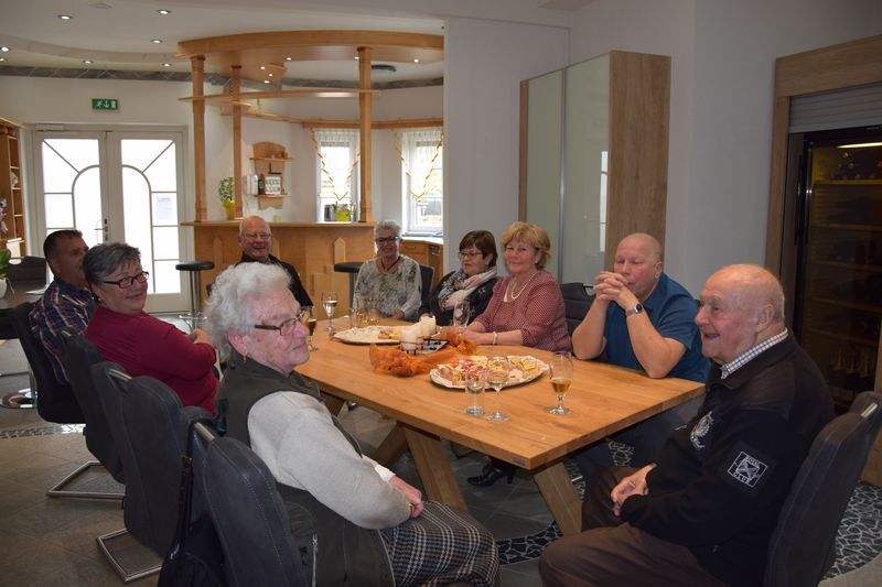 Eine Gruppe von Leuten sitzt in einem Wohnzimmer um einen Tisch herum.