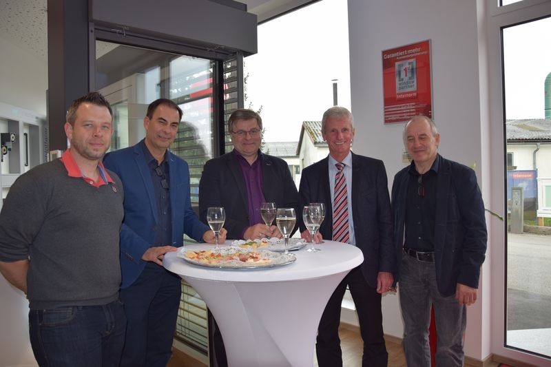 Eine Gruppe Männer steht mit Weingläsern um einen Tisch herum.