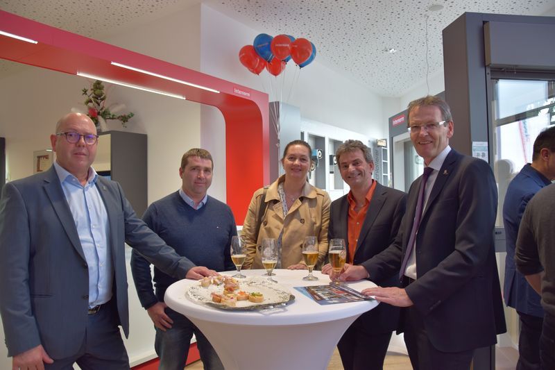 Eine Gruppe von Menschen steht mit Weingläsern um einen Tisch herum.