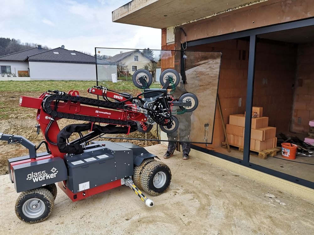 Roter Glasheberoboter platziert Fensterscheiben auf einer Baustelle. Ein Arbeiter hilft.