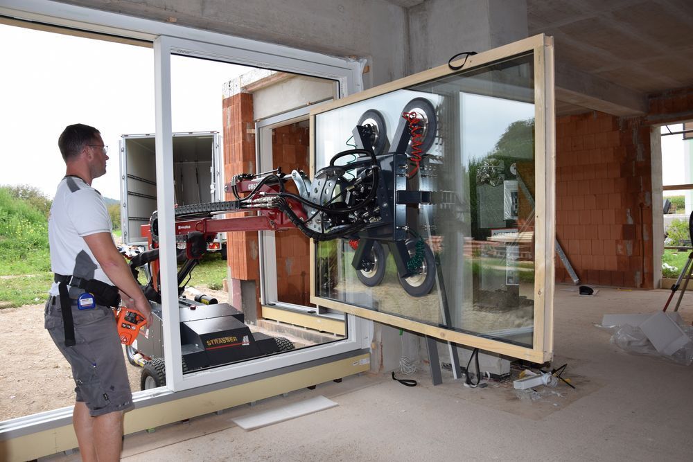 Mann verwendet eine Maschine, um ein großes Fenster in ein im Bau befindliches Gebäude einzubauen.