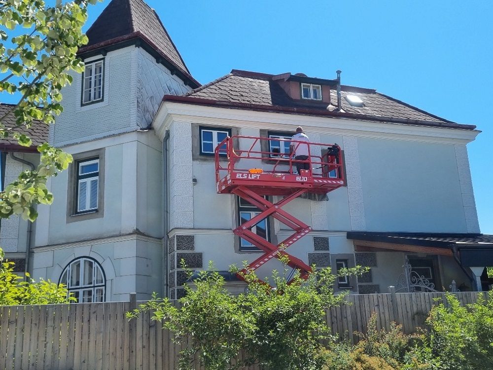 Ein Mann steht auf einer roten Scherenhebebühne an der Seite eines Gebäudes.