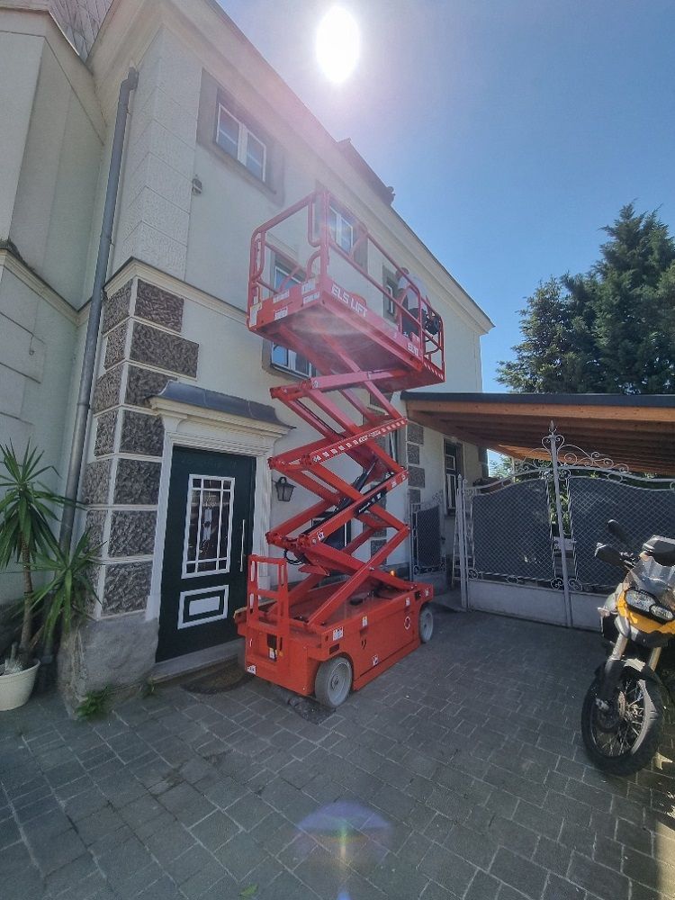 Vor einem Gebäude steht eine rote Scherenbühne.