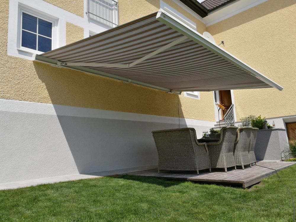 Eine große Markise überdacht einen Terrassenbereich vor einem Haus