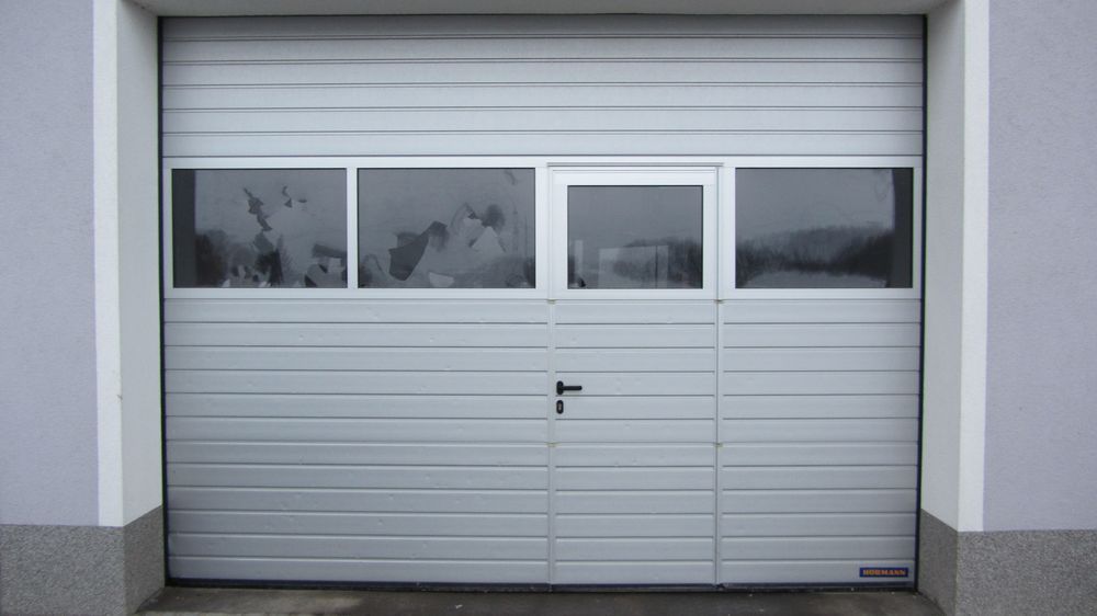 Ein weißes Garagentor mit drei Fenstern und einer Tür