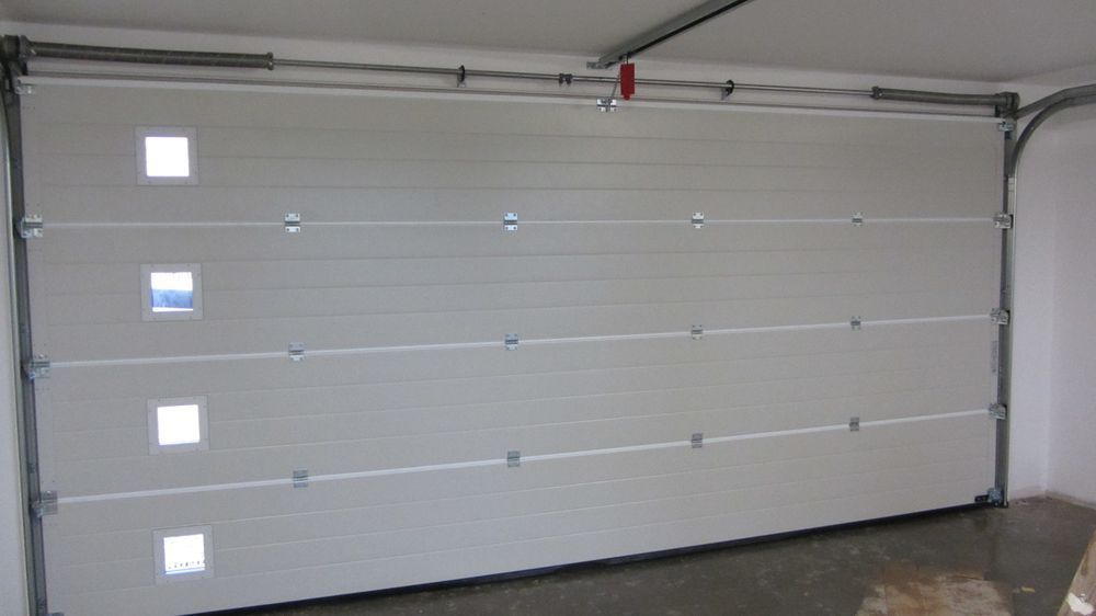 In einer Garage steht ein weißes Garagentor mit quadratischen Fenstern offen.