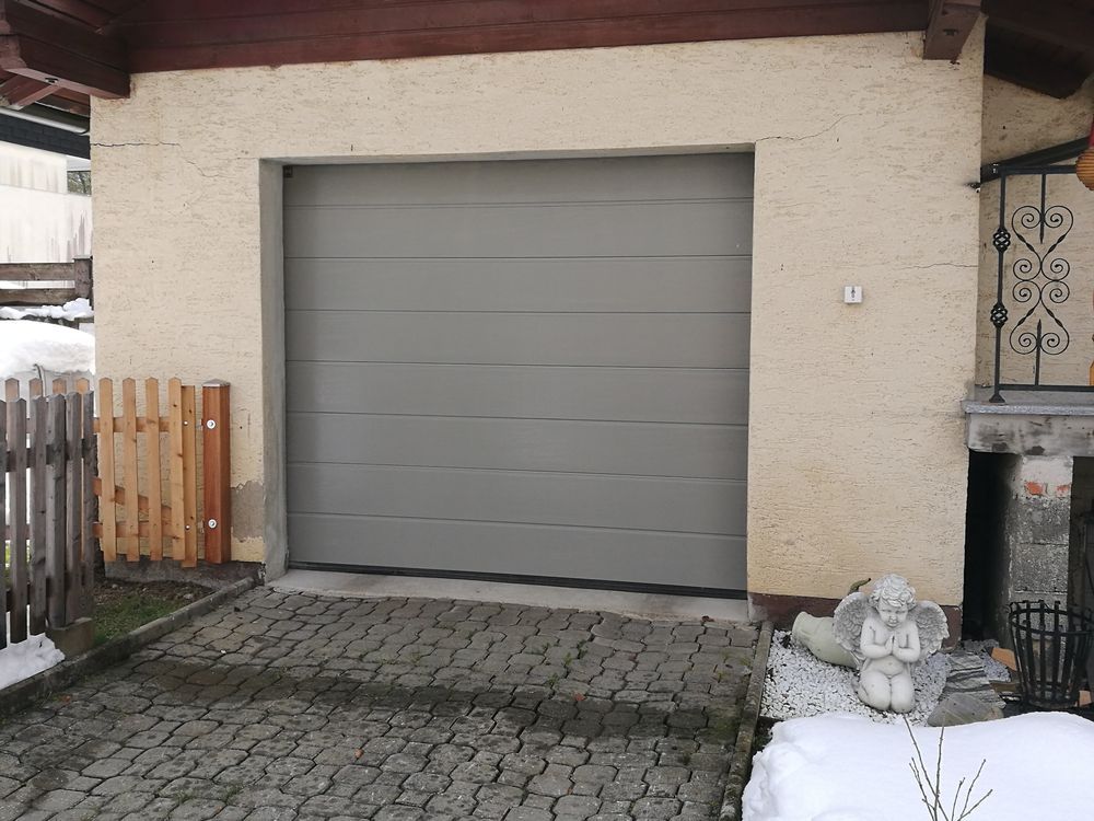 Vor einem Haus steht ein graues Garagentor offen