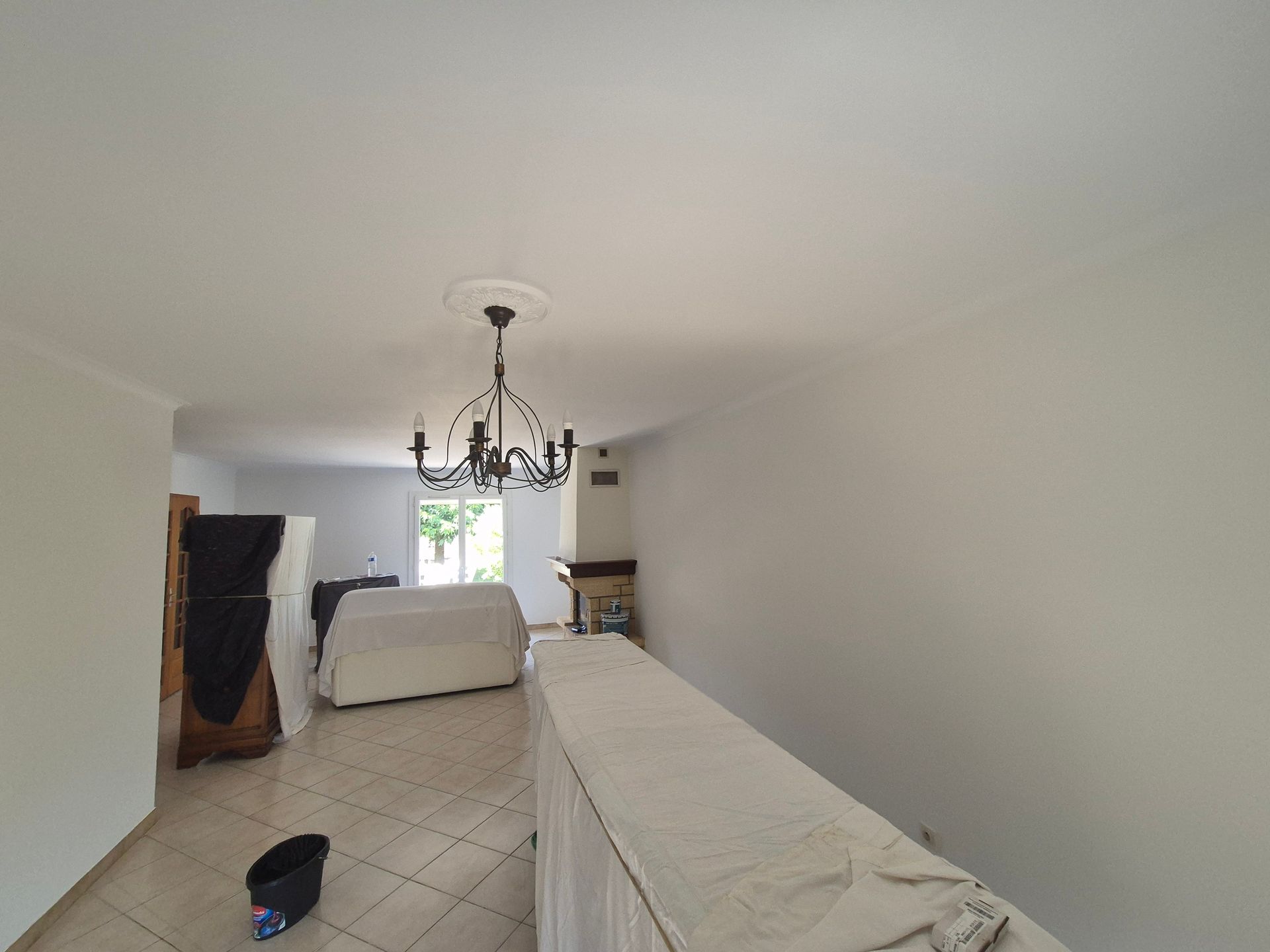 Salon repeint en blanc avec un bar et un canapé sous des protections