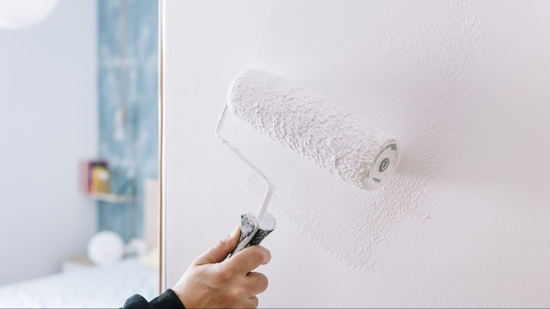 Main de quelqu'un en train de peindre avec un rouleau de la peinture blanche sur un mur