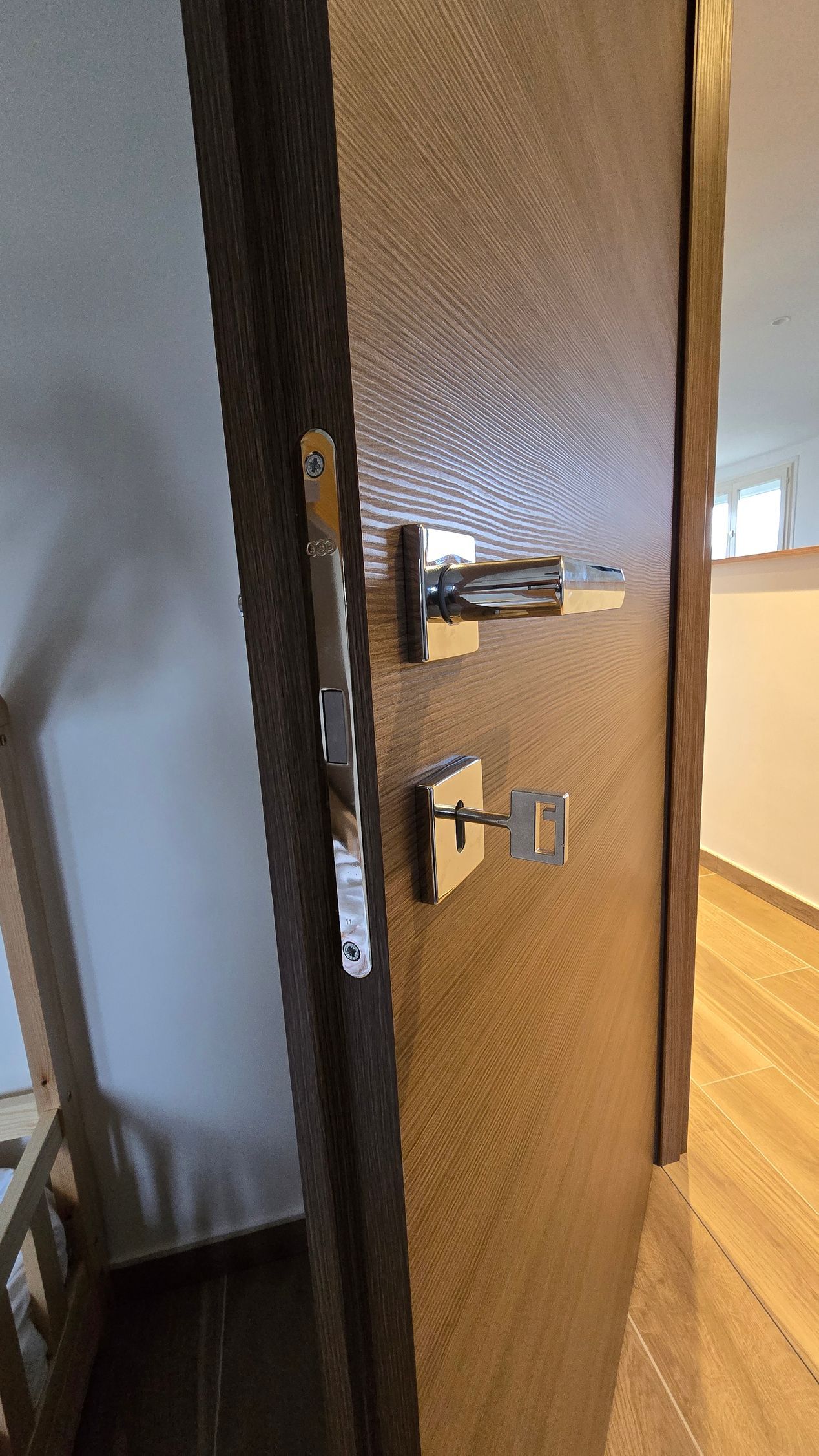 Porte marron avec poignée argentée et clé dans la serrure, menant à une pièce avec parquet.