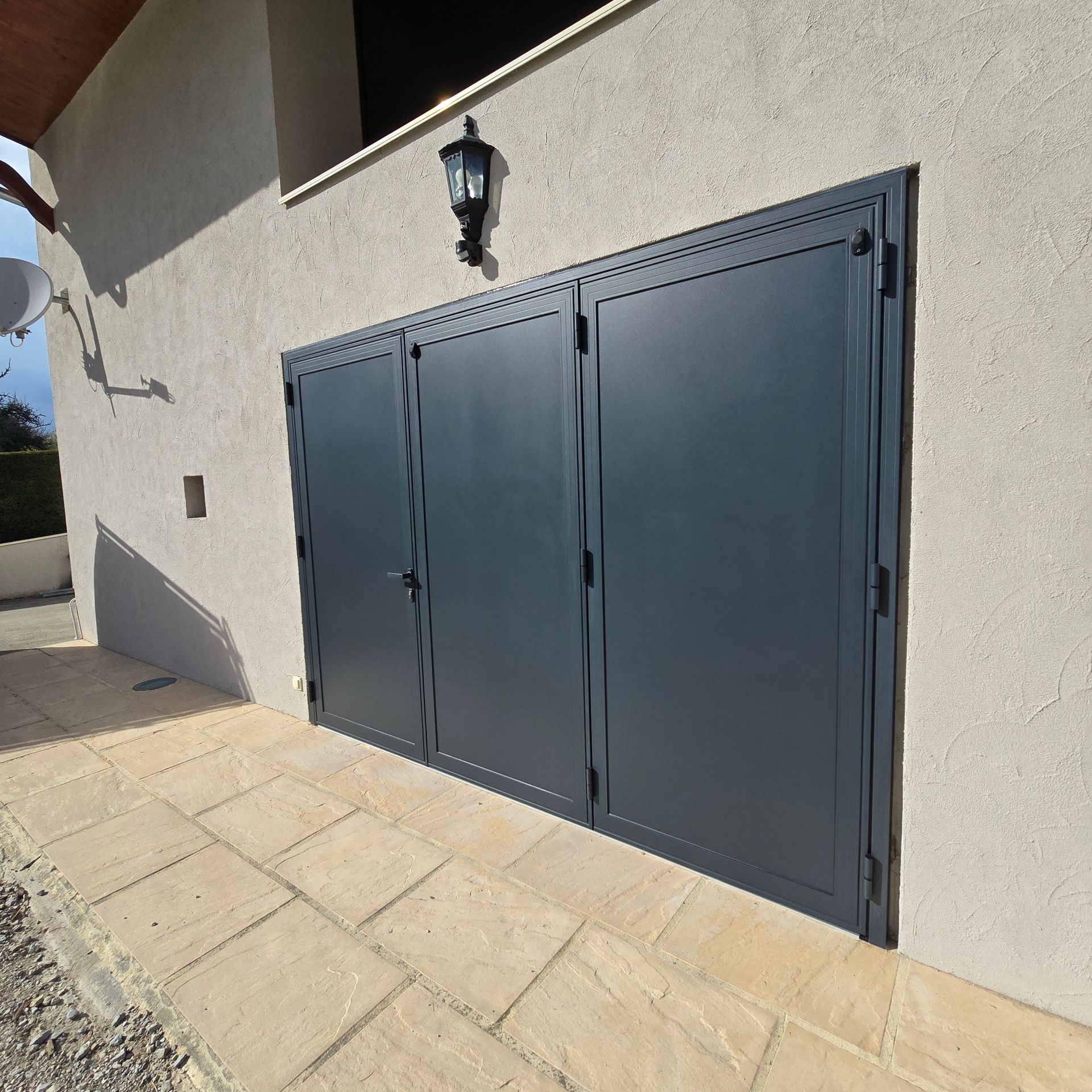 Portes de garage grises sur un bâtiment en stuc de couleur claire avec une allée en pierre.