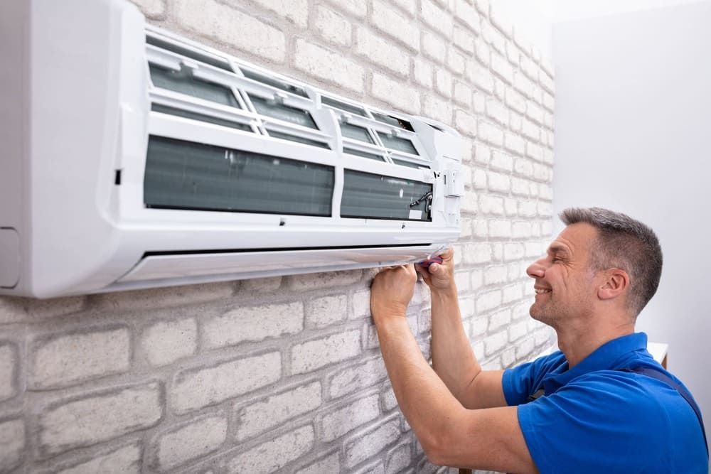 Ein Mann installiert eine Klimaanlage an einer Backsteinmauer.