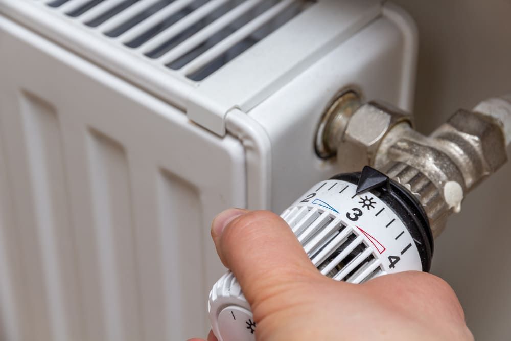 Eine Person stellt einen Thermostat an einem Heizkörper ein.