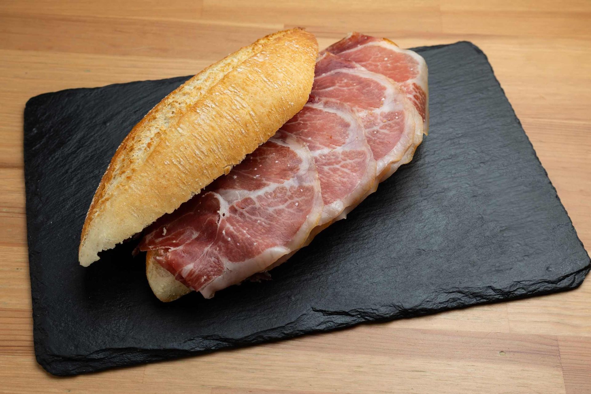 Un sándwich está sobre una tabla de cortar negra sobre una mesa de madera.