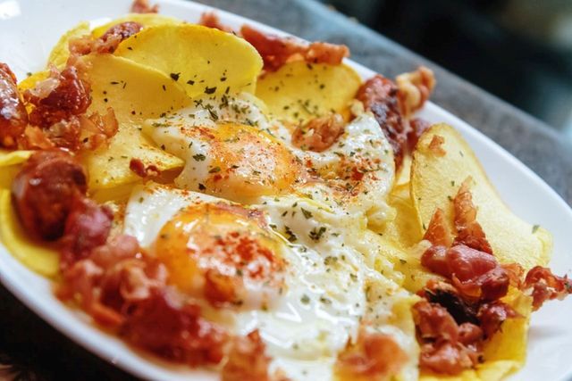 Un plato de comida con huevos, patatas y tocino en una mesa.