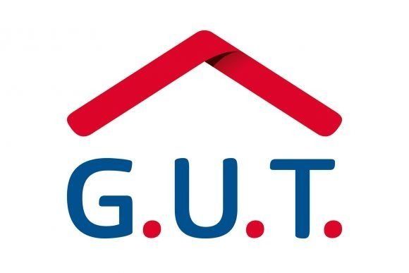 Das Logo von „GUT“ ist vor dem Hintergrund eines roten Hauses abgebildet. Text und Umriss sind blau.