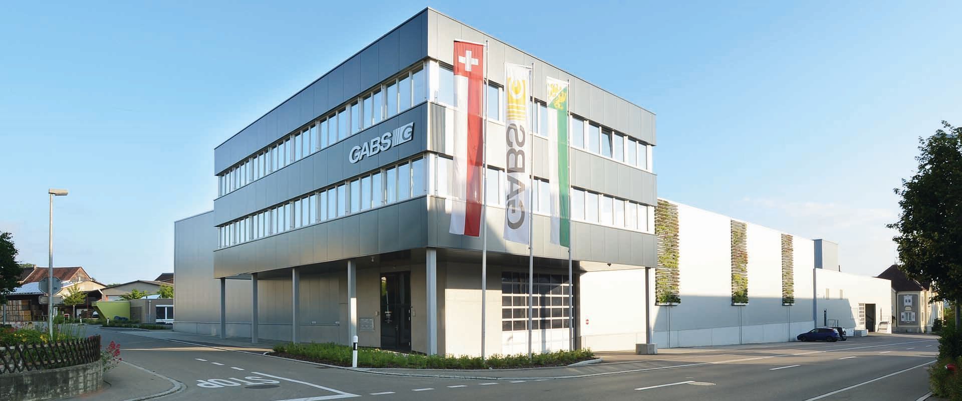 Modernes Gebäude mit Schweizer Flagge und Firmenbannern davor. Außenansicht, tagsüber.