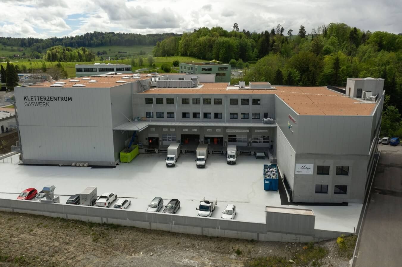 Modernes Industriegebäude mit Lastwagen an Laderampen, grünem Bus und draußen geparkten Autos. Neubau unter Beteiligung der Kather Sanität und Heizung GmbH