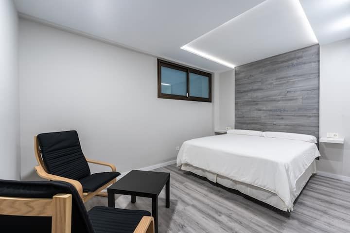 Un dormitorio con una cama, silla, mesa y ventana.
