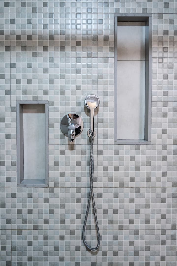 Un cabezal de ducha cuelga de una pared de azulejos en un baño.