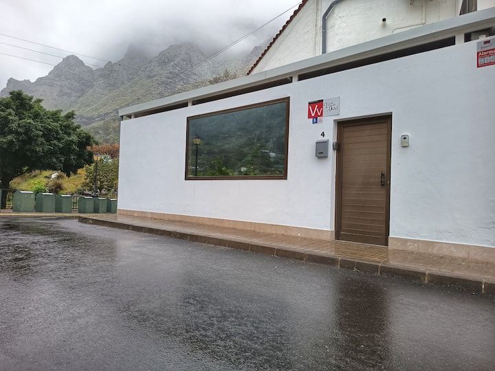 Un edificio blanco con una puerta marrón y una ventana grande en un día lluvioso.