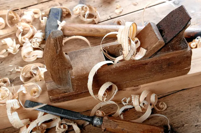 Ein Holzhobel liegt auf einem Stück Holz auf einem Holztisch.