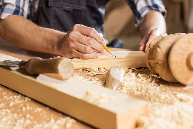 Ein Mann misst ein Stück Holz mit einem Bleistift.