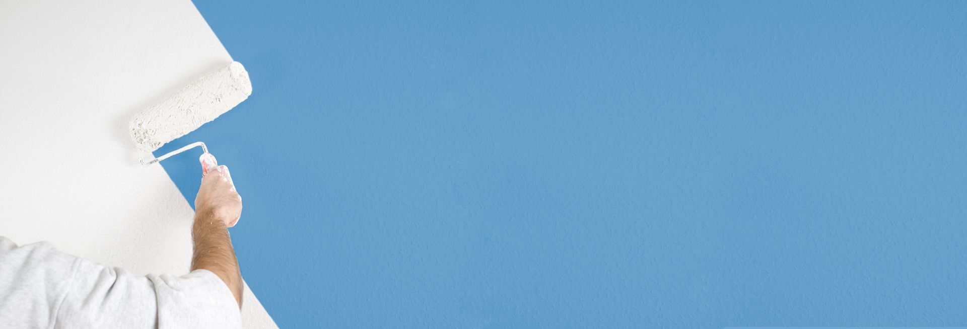 Eine Person streicht eine weisse Wand mit einer Farbrolle blau.