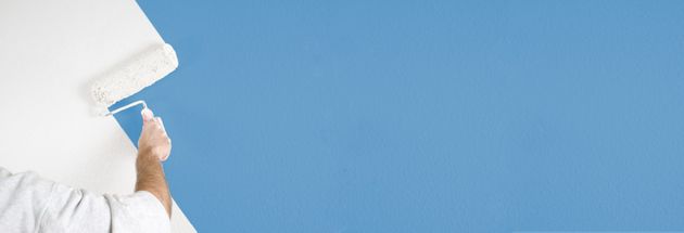 Eine Person streicht eine weisse Wand mit einer Farbrolle blau.
