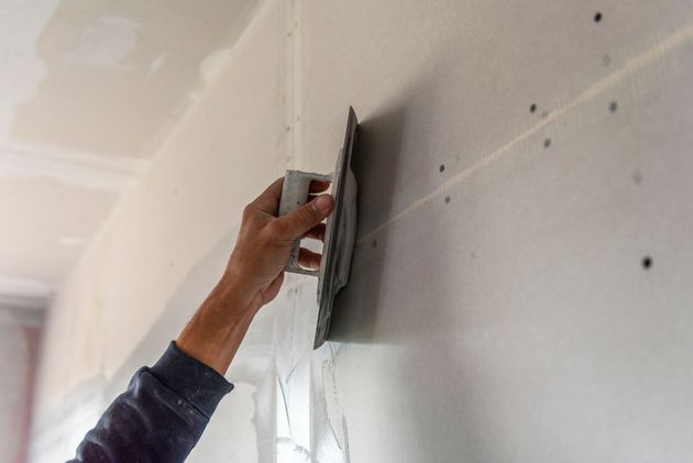 Auftragen von Spachtelmasse per Hand mit einer Kelle auf eine Gipskartonfuge an einer Wand.