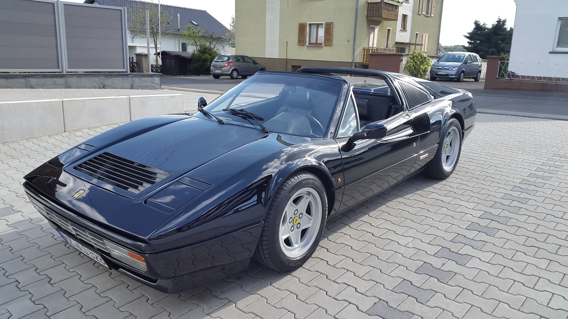 Ein schwarzer Sportwagen ist auf einer gepflasterten Auffahrt vor einem Haus geparkt.