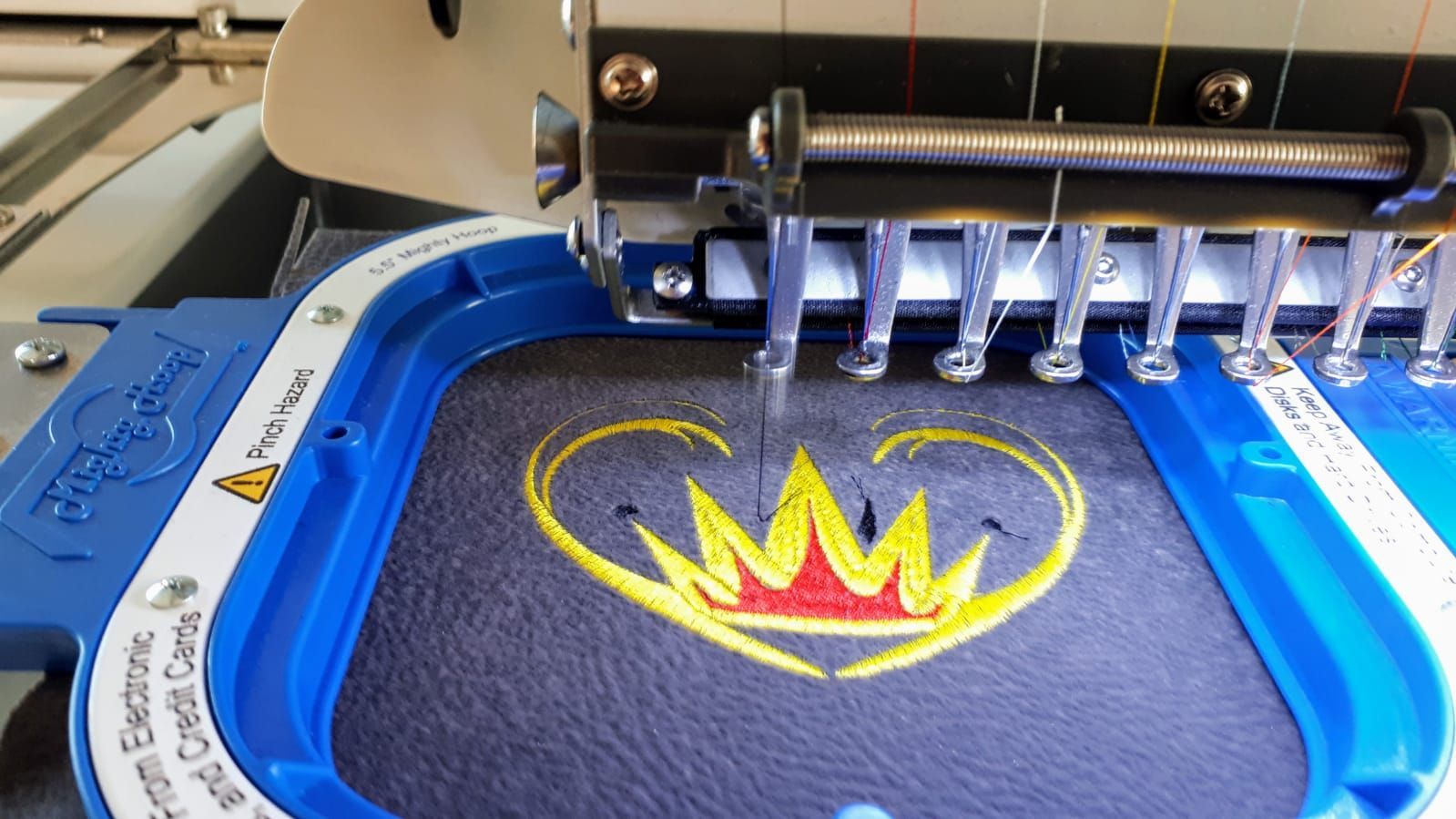 Eine Maschine stickt ein Herz mit einer Krone darauf.