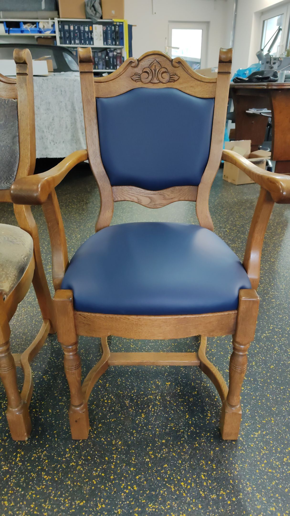 Auf einem schwarzen Boden steht ein Holzstuhl mit blauem Kissen.