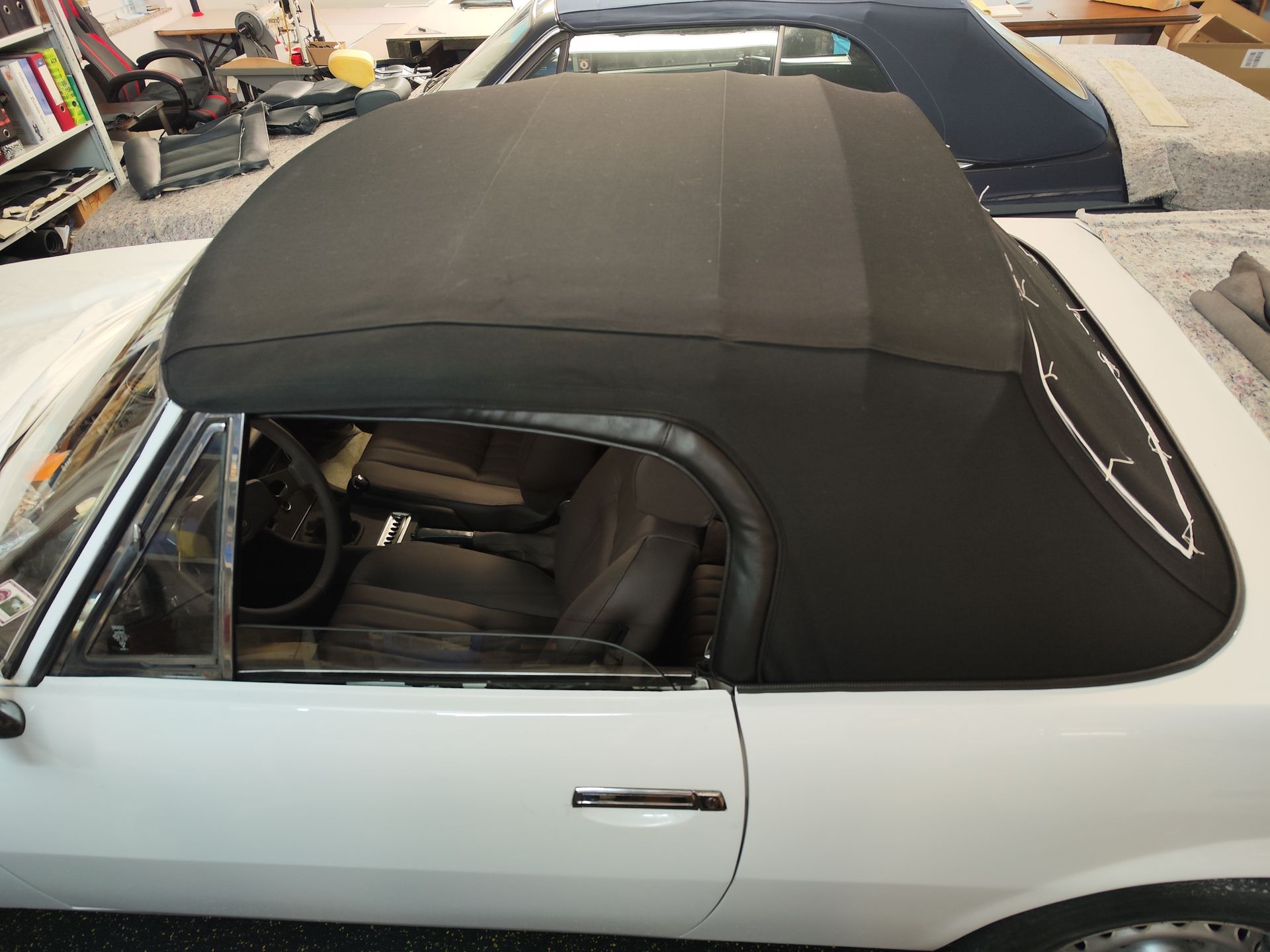 Ein weißes Cabrio mit schwarzem Verdeck steht in einer Garage.