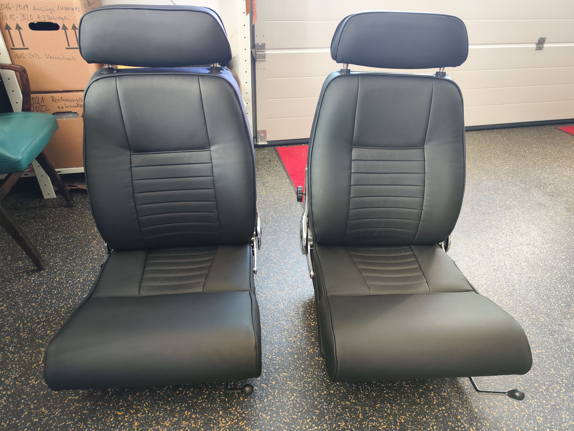 Zwei schwarze Lederautositze stehen nebeneinander in einer Garage.