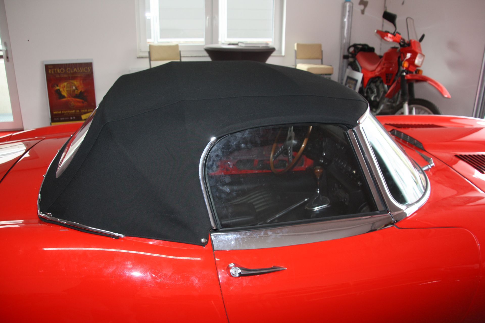 Ein roter Sportwagen mit schwarzem Dach steht in einer Garage